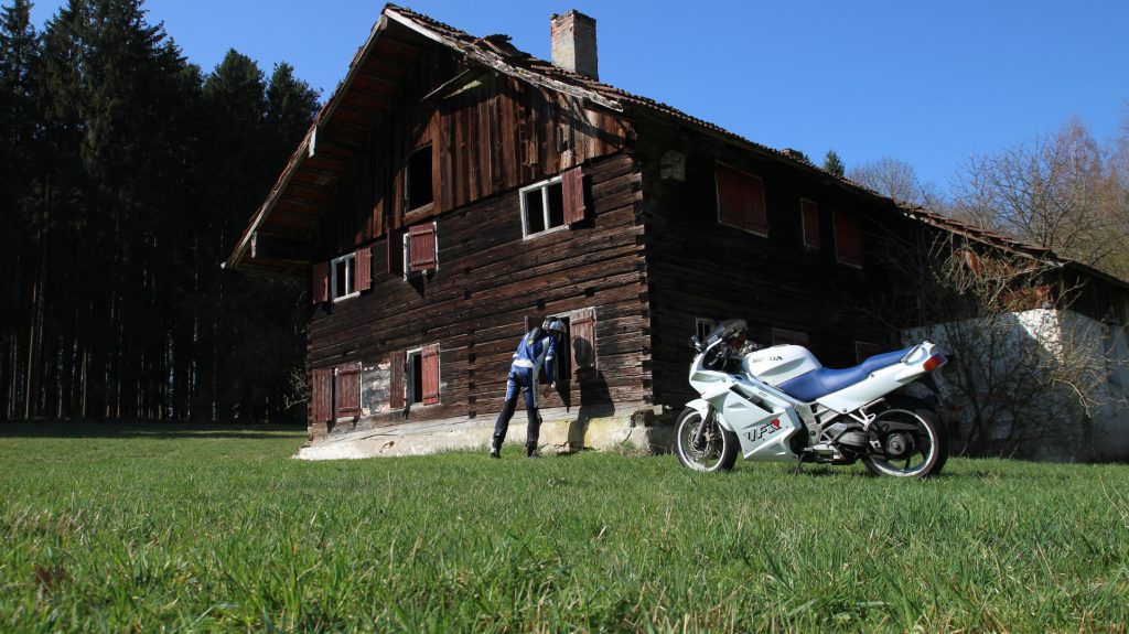 Motorrad vor Bauernhof Thomasbach. Der Fahrer schaut durchs Fenster.