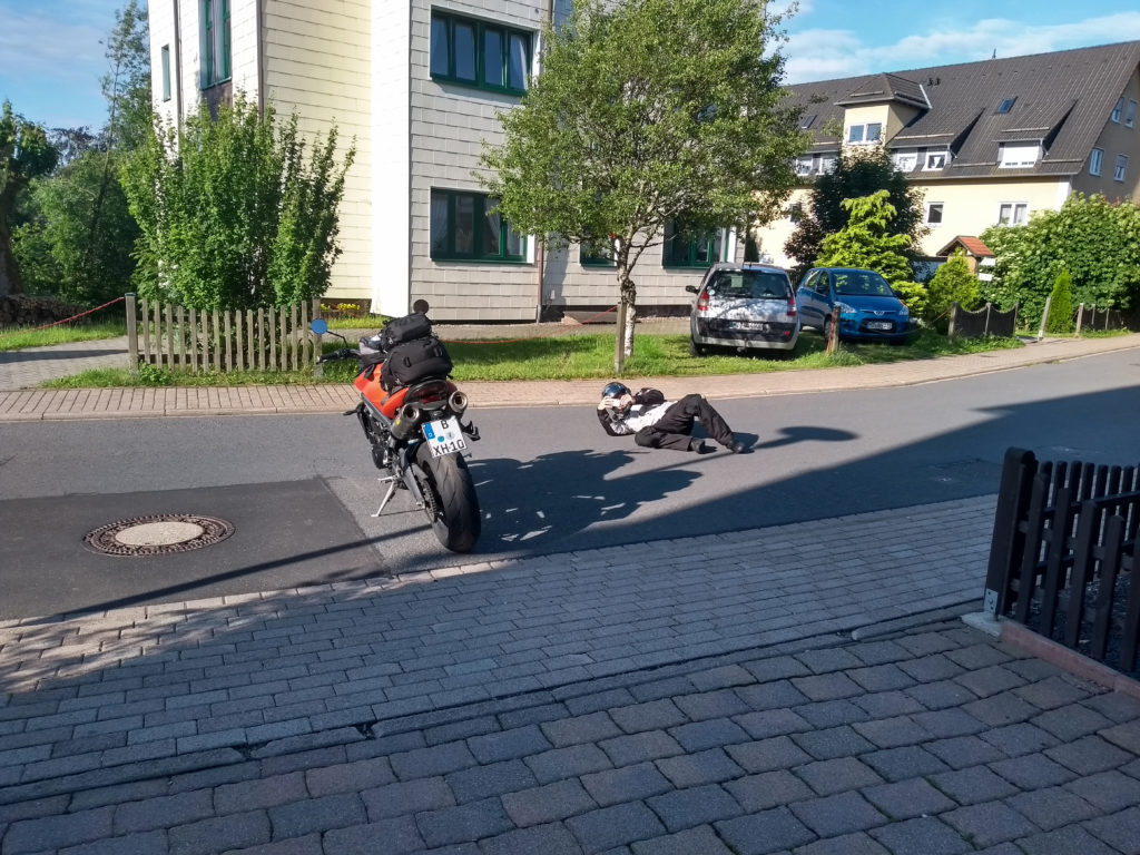 Motorradfahrer liegt fotografierend auf der Straße.