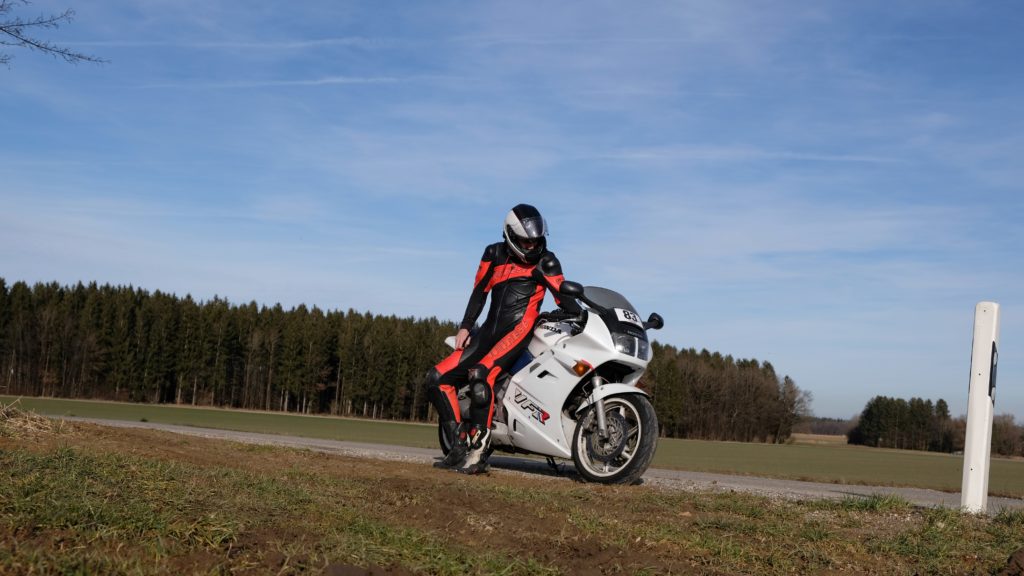 Motorradfahrer sitzt seitlich auf stehendem Motorrad